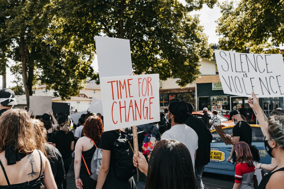 Menschen auf einer Demonstration halten Schilder mit den Aufschriften "TIME FOR CHANGE" und "SILENCE IS VIOLENCE" hoch.