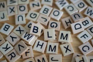 Symbolbild zur Fortbildung Einfache und Leichte Sprache in der Beteiligung junger Menschen Kleine Holzplättchen mit unterschiedlichen Buchstaben liegen kreuz und quer neben- und übereinander.
